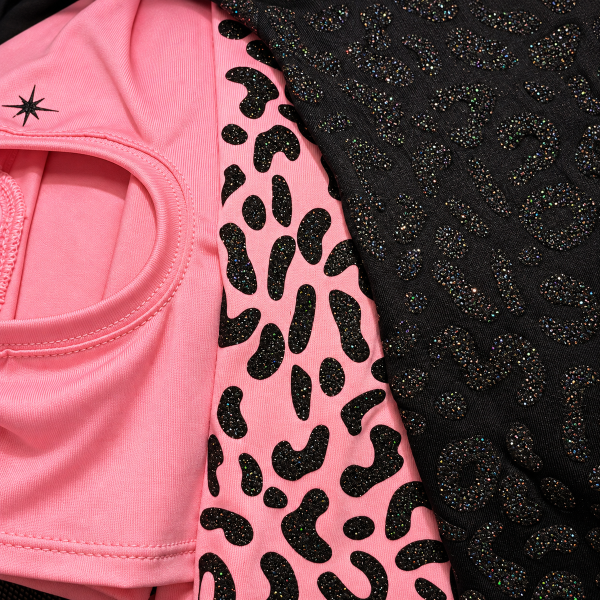 Close-up of a pink garment with a black leopard print pattern and a black textured embellished panel, shown against a dark background.